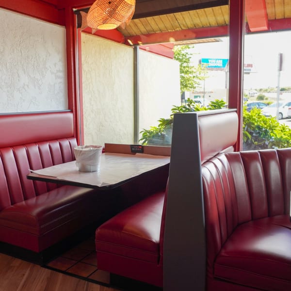 Red vinyl booths and tables with paper coverings inside a restaurant with large windows.