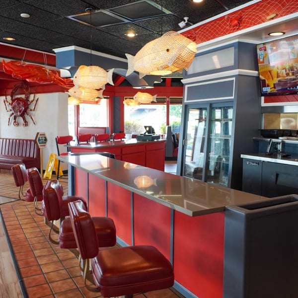 A vibrant red and black restaurant interior with a bar, booths, and fish-shaped light fixtures.