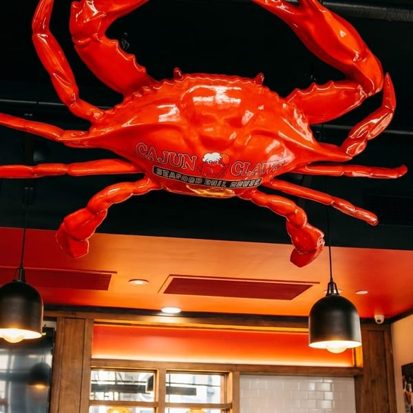 Large red crab sculpture with "Cajun Claws Seafood Boil House" text hanging from a black ceiling.