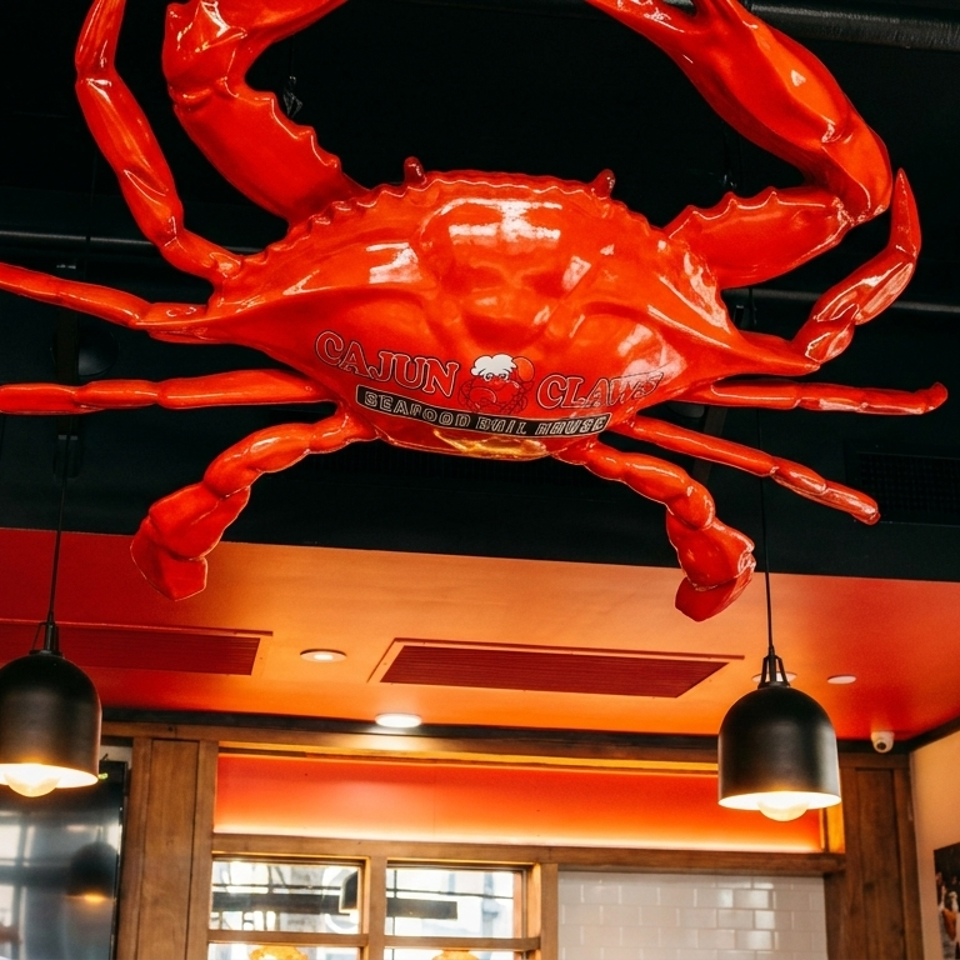 Large red crab sculpture with "Cajun Claws Seafood Boil House" text hanging from a black ceiling.