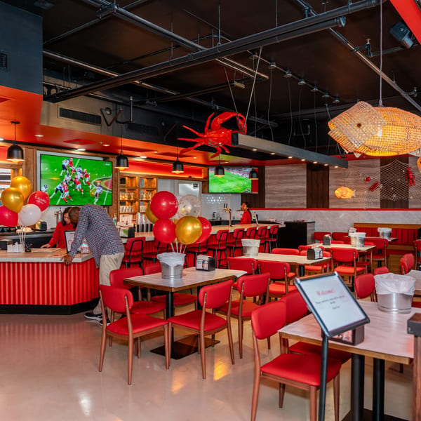 Spacious restaurant interior with red chairs, tables, a bar, and nautical decor, including fish lamps.