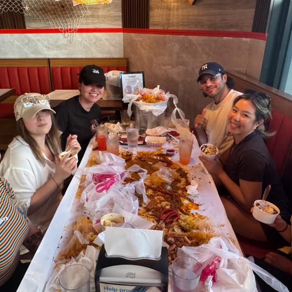Six smiling friends gathered around a table covered in seafood boil remnants and drinks.