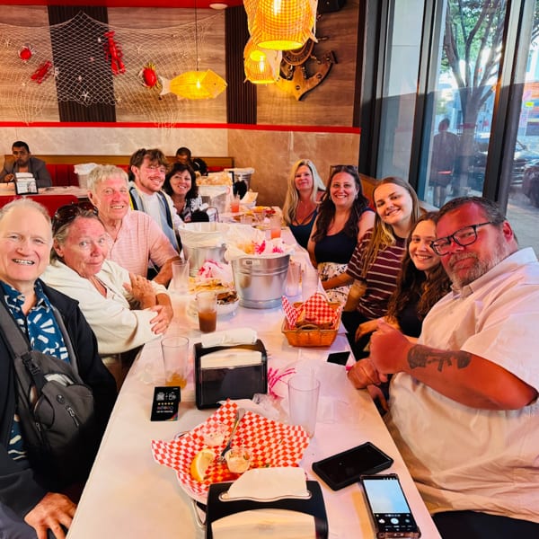 A large group of people smiling and sitting around a long table in a seafood restaurant.