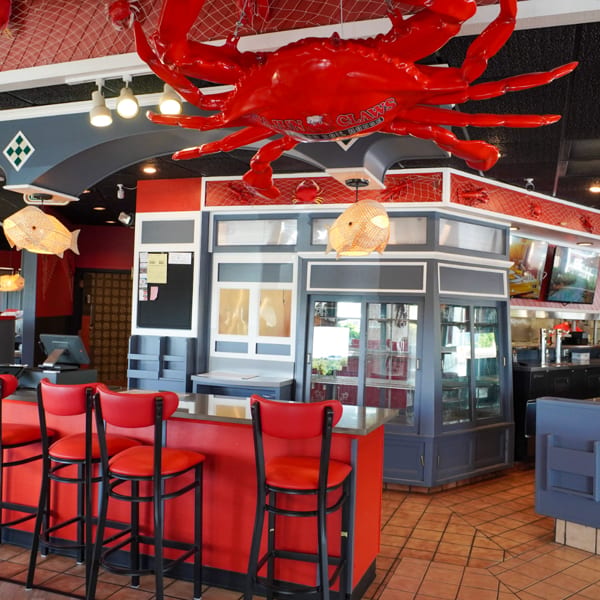 Restaurant interior with red bar stools, a large red crab decoration, and nautical-themed decor.