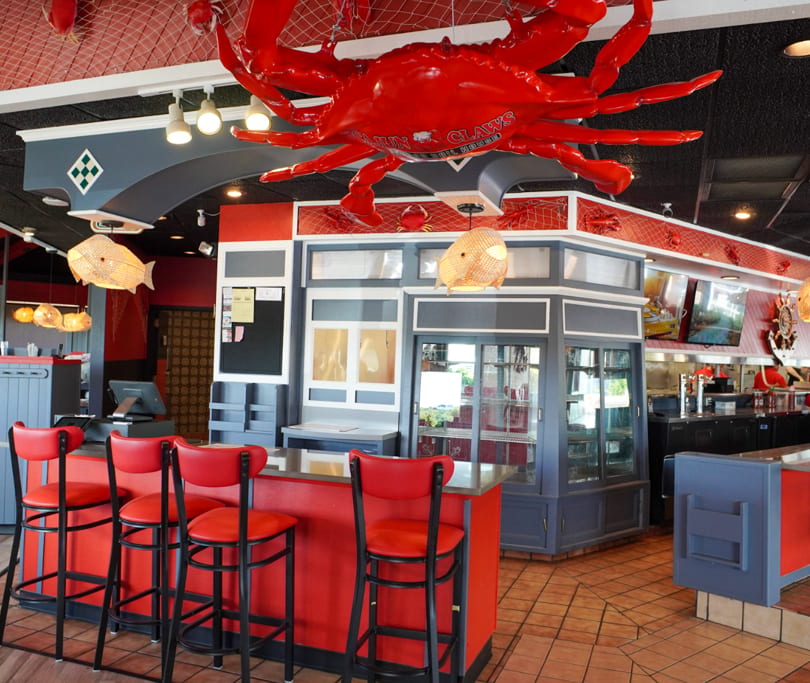 Restaurant interior with a large red crab decoration, red bar stools, and nautical-themed decor.