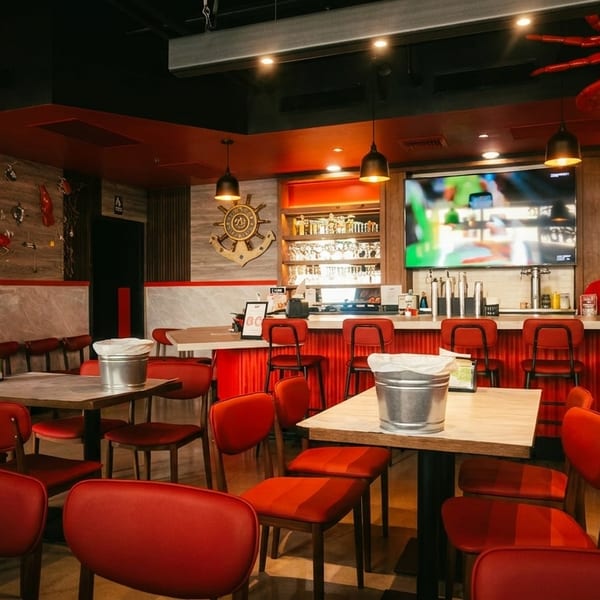 Interior of a seafood restaurant with red chairs, wooden tables, a bar, and crab decorations.