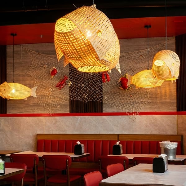 Restaurant interior with red booths, tables, and nautical decor including fish-shaped lights and a ship's wheel.