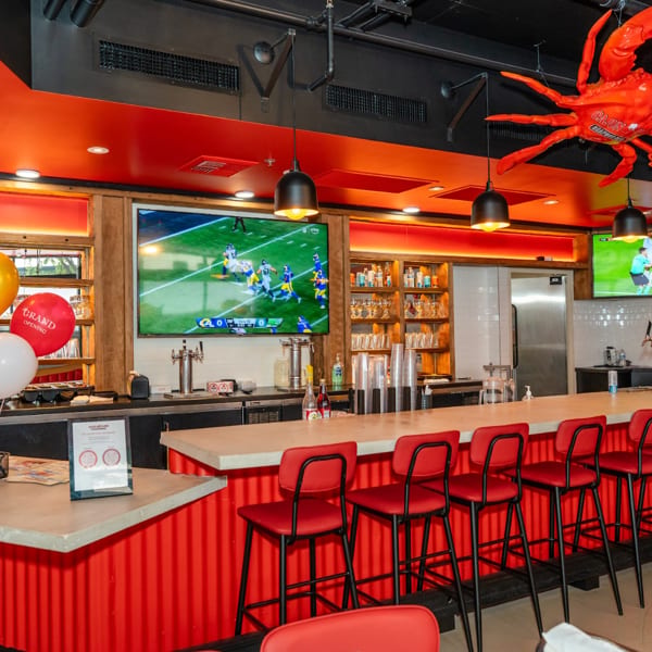 Vibrant red and black restaurant interior with a long bar, red stools, TVs, and a large crab decor.