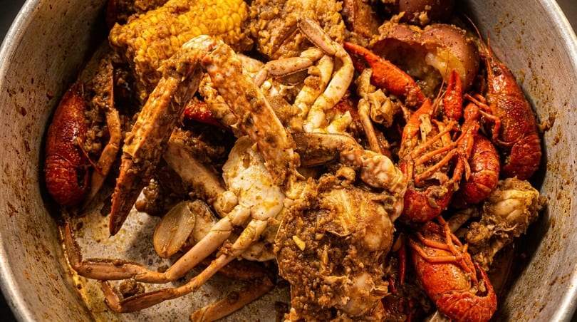 Close-up of a seafood boil with crabs, crawfish, corn, and potatoes in a metal pot.