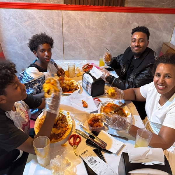 Four people, including two children, happily eating seafood with gloves at a restaurant table.