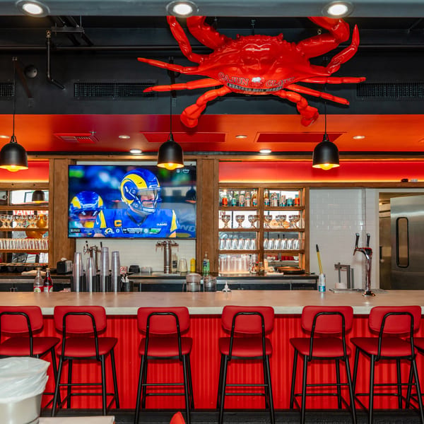 A vibrant bar with red stools, a large TV, and a giant red crab decoration on the ceiling.