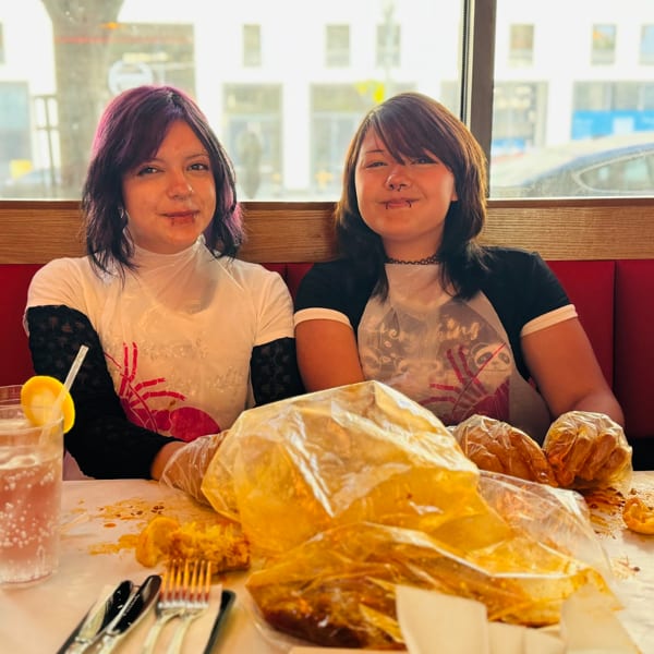 Two young women in plastic bibs and gloves, smiling after eating a messy seafood boil.