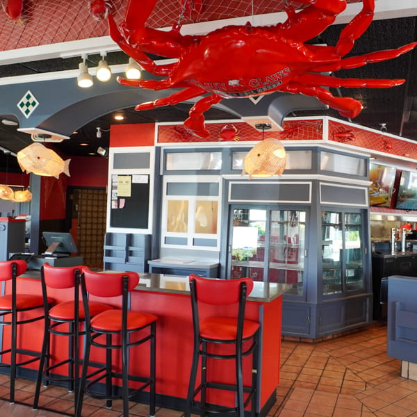Interior of a Cajun Claws restaurant with red bar stools, a large red crab decoration, and nautical decor.