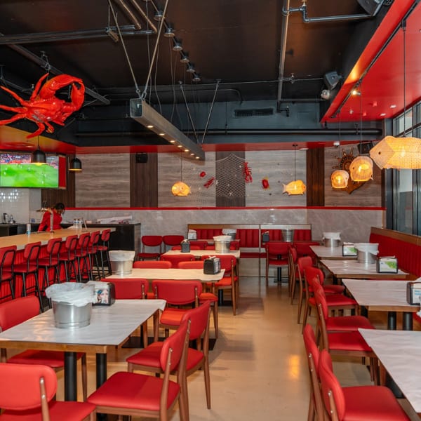 Spacious, empty restaurant interior with red chairs, white tables, a bar, and seafood-themed decor.