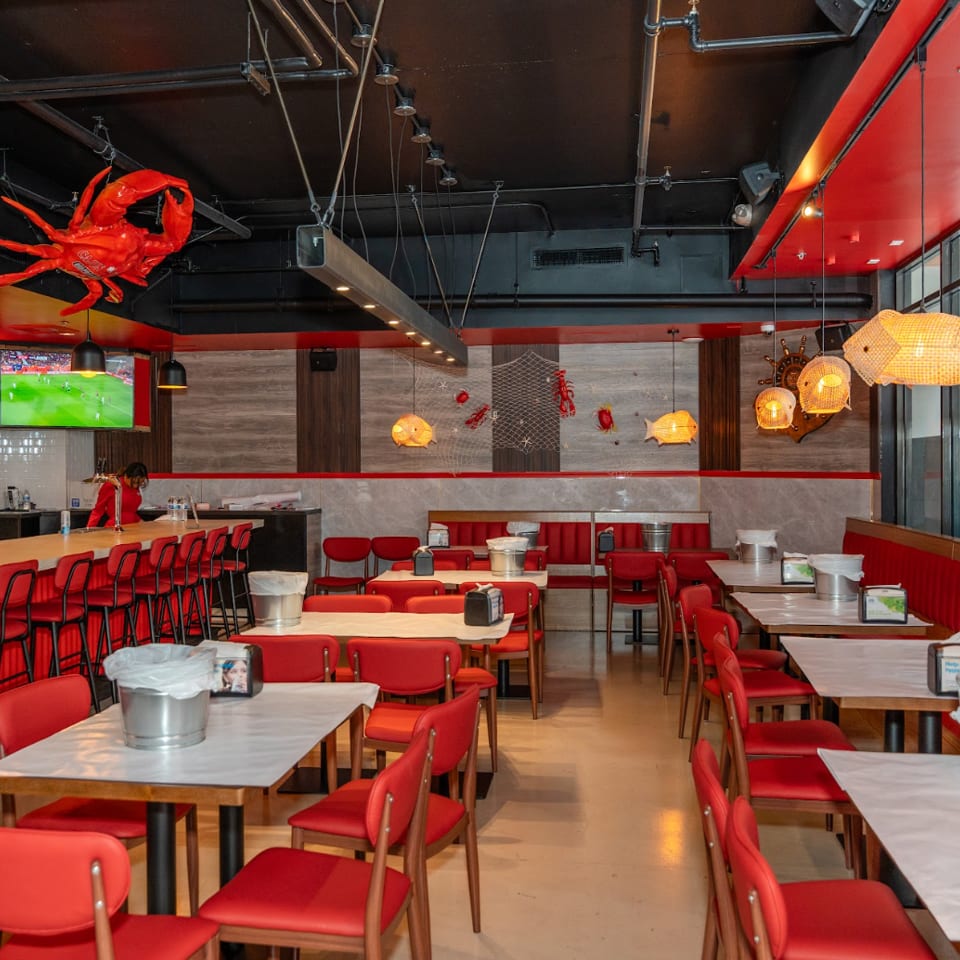 Spacious, empty restaurant interior with red chairs, white tables, a bar, and seafood-themed decor.