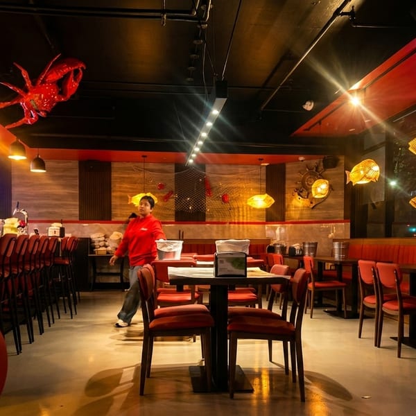 Restaurant interior with red decor, bar seating, dining tables, and a person walking.