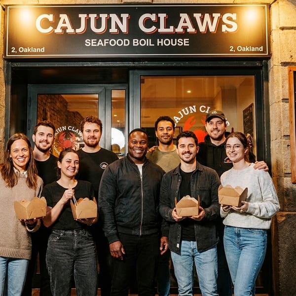 Eight smiling staff members stand outside Cajun Claws Seafood Boil House, holding takeout boxes.