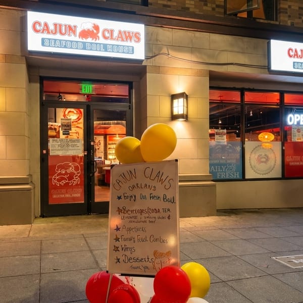 Exterior of Cajun Claws Seafood Boil House at night, with illuminated signs and a menu board.