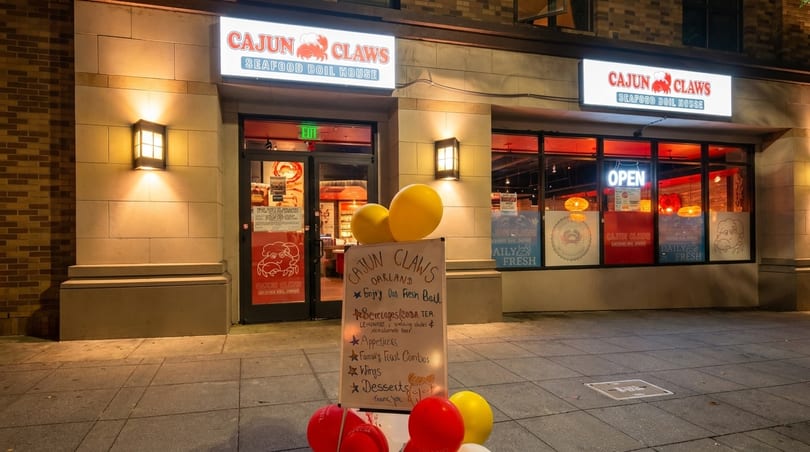 Exterior of Cajun Claws Seafood Boil House at night, with illuminated signs and a menu board.