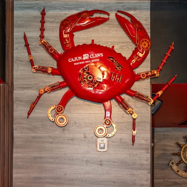 Large red crab art with gears and "Cajun Claws Seafood Boil House" text on a gray wall.